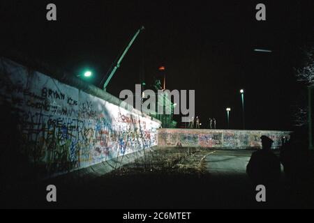 Ostdeutsche Wachen beobachten, wie ein Kran bereitet einen Abschnitt der Berliner Mauer am Brandenburger Tor zu entfernen. Stockfoto