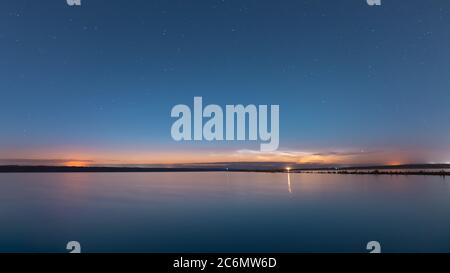 Natürliche Nachtlandschaft mit einem Sternenhimmel auf dem See, vor der Dämmerung der Sonne in der Ferne lila Wolken. Stockfoto