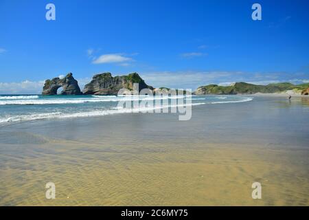 Wunderschöne neuseeländische Seestraine am Strand von Wharariki. Archway-Inseln. Zwei Personen stehen auf der rechten Seite. Südinsel. Stockfoto