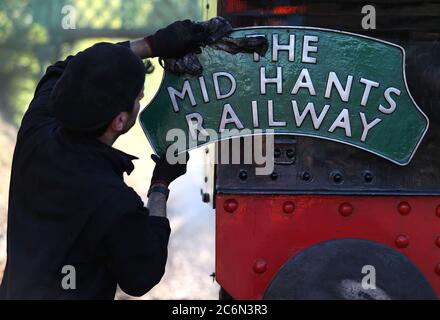 Ein Schild für die Mid Hants Railway wird auf der Rückseite der British Railways Ivatt Class 2MT Tank Engine 41312 am Bahnhof von Ropley gereinigt, da die Mid Hants Railway, auch bekannt als Watercress Line, sich nach der Lockerung der Sperrbeschränkungen in England darauf vorbereitet, der Öffentlichkeit wieder zu öffnen. Stockfoto