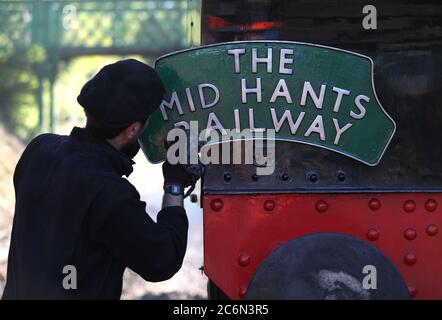 Ein Schild für die Mid Hants Railway wird auf der Rückseite der British Railways Ivatt Class 2MT Tank Engine 41312 am Bahnhof von Ropley gereinigt, da die Mid Hants Railway, auch bekannt als Watercress Line, sich nach der Lockerung der Sperrbeschränkungen in England darauf vorbereitet, der Öffentlichkeit wieder zu öffnen. Stockfoto