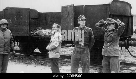 Die Übergabe des Konzentrationslagers Dachau an amerikanische Streitkräfte der 42. Infanterie-Division der Armee, 29. April 1945 in Dachau, Deutschland. Der deutsche Offizier, der als Kommandant des Lagers dient, zweiter von rechts, SS-Oberstleutnant Heinrich Wickert (Wicker), wird rechts von dem Schweizer Vertreter des Internationalen Roten Kreuzes, Dr. Victor Maurer, begleitet. Die Gruppe wurde neben dem „Todeszug“ von Triebwagen fotografiert, die die Toten der vor der Lagerübergabe nach Dachau überführten Personen hielten. Amerikanische Soldaten der 7. Armee der USA, einschließlich der 42. Infanterie und 45. Infanterie und 20. Panzerdivisionen Stockfoto