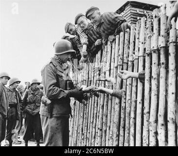 Der US-Armeekorporal Larry Matinsk legt den frisch befreiten Gefangenen am 30. April 1945 Zigaretten in die ausgestreckten Hände hinter einer Lagerstätte im KZ Allach bei Dachau. Ebenfalls abgebildet sind die US-Soldaten Arthur Toratti und George Babel (zweiter und dritter von links). Allach war ein Unterlager des Konzentrationslagers Dachau. An der Befreiung des Unterlagers nahmen amerikanische Soldaten der 7. Armee der USA Teil, darunter Mitglieder der 42. Infanterie und der 45. Infanterie und der 20. Panzerdivision. Das Hauptkonzentrationslager Dachau hatte mehr als 120 Nebenlager in der Gegend Stockfoto