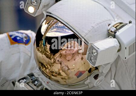 (19. - 27. Dezember 1999) - das Cargo Bay and Crew Module des Space Shuttle Discovery und der Horizont der Erde spiegeln sich im Helmvisier eines der Weltraumastronauten auf STS-103 wider. Die Astronauten Steven L. Smith, John M. Grunsfeld, C. Michael Foale und Claude Nicollier nahmen an drei Tagen an der dritten Inspektion des Hubble Space Telescope (HST) der NASA Teil. Stockfoto