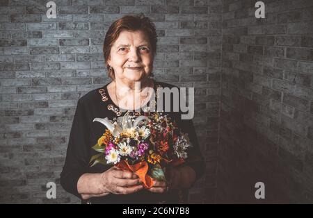 Ernte ältere Frau mit Blumen. Nicht erkennbare ältere Dame mit eingewickelten Blumenstrauß während der Feiertagsfeier Stockfoto