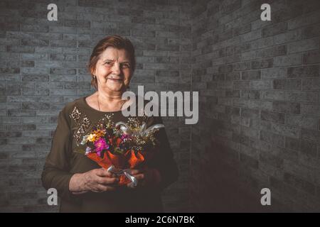 Ernte ältere Frau mit Blumen. Nicht erkennbare ältere Dame mit eingewickelten Blumenstrauß während der Feiertagsfeier Stockfoto