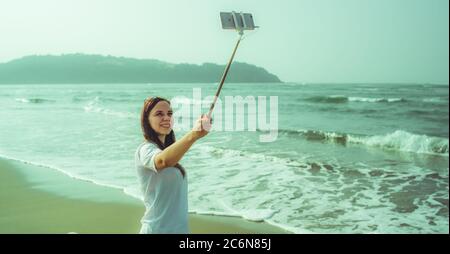 Glückliche Hündin, die Selfie in der Nähe des Meeres macht. Von oben froh Frau mit Monopod mit Smartphone Selfie in der Nähe winkenden Meer am Strand zu nehmen Stockfoto