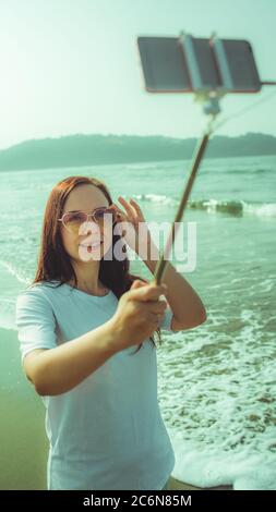 Glückliche Hündin, die Selfie in der Nähe des Meeres macht. Von oben froh Frau mit Monopod mit Smartphone Selfie in der Nähe winkenden Meer am Strand zu nehmen Stockfoto