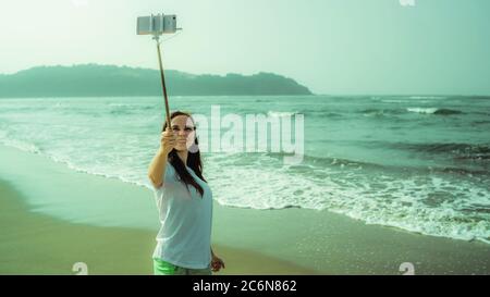 Glückliche Hündin, die Selfie in der Nähe des Meeres macht. Von oben froh Frau mit Monopod mit Smartphone Selfie in der Nähe winkenden Meer am Strand zu nehmen Stockfoto