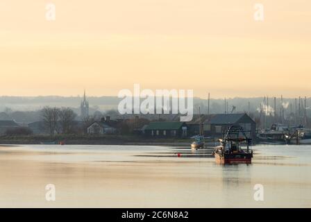 Boote auf Faversham Creek von Oare Marshes in Kent genommen. In der Ferne ist die gotische Kirche der Heiligen Maria der Nächstenliebe von Faversham zu sehen. Stockfoto