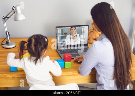 Hausarzt online. Mutter und Tochter hören der Arztkonsultation zu und haben eine Videokonferenz im Zimmer. Stockfoto