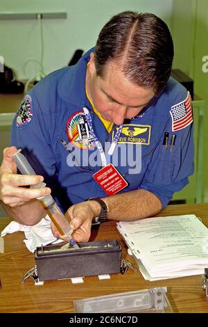 STS-95 Mission Specialist Stephen K. Robinson spritzt Wasser in die Basis des Saatbehälters, wo Pflanzen während der kommenden Mission wachsen werden. Dies ist Teil des Experiments Biological Research in Canisters (BRIC), das an der SPACEHAB Payload Processing Facility in Cape Canaveral, Florida, durchgeführt wird. Dieses Experiment wird in SPACEHAB in der Nutzlastbucht des Discovery fliegen. STS-95 soll am 29. Oktober 1998 von Pad 39B bei KSC starten. Die Mission umfasst auch Forschungslasten wie die Spartan Solar-Observing einsetzbare Raumsonde, das Hubble Space Telescope Orbital Systems Test Platform, das Internat Stockfoto