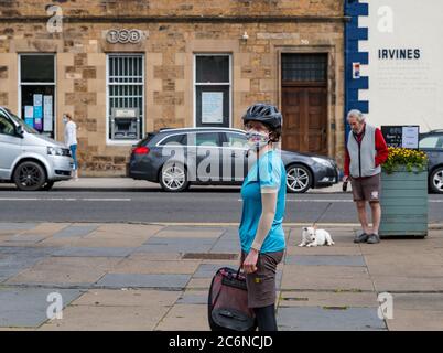 Haddington, East Lothian, Schottland, Großbritannien, 11. Juli 2020. Bauernmarkt startet in Phase 3 wieder: Der beliebte monatliche Markt im Freien wird zum ersten Mal seit der Aussperrung abgehalten, wobei Einheimische daran interessiert sind, lokale Lebensmittelproduzenten zu unterstützen. Obwohl nicht zwingend im Freien, die meisten Menschen tragen Gesichtsmasken. Soziale Distanzierungsmaßnahmen sind vorhanden. Im Bild: Eine Radfahrerin mit Gesichtsmaske wartet in der gesellschaftlich distanzierten Schlange Stockfoto