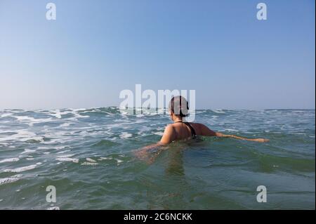 Junge Frau im schwarzen Badeanzug verbringt Zeit im Meer. Erwachsene Dame schwimmt in Richtung der Wellen. Stockfoto