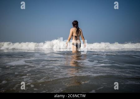 Junge Frau im schwarzen Badeanzug verbringt Zeit im Meer. Erwachsene Dame schwimmt in Richtung der Wellen. Stockfoto