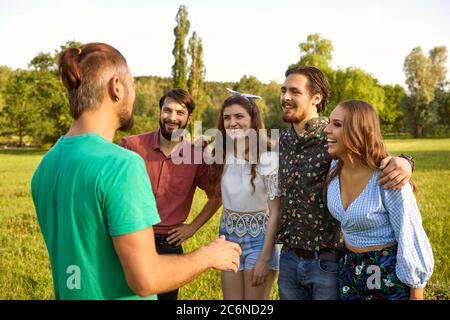 Gruppe von fröhlichen jungen Menschen kommunizieren im Freien am Sommertag. BFFs Spaß haben zusammen in der Landschaft Stockfoto