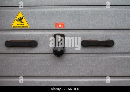 Textur eines Aluminium Garagentor. Mit Griff und Schloss und einem Aufkleber mit einer Warnung „Video überwacht“ Stockfoto