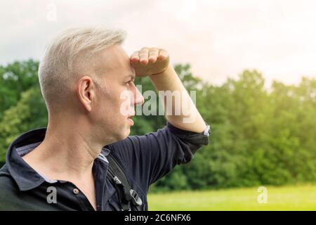 Der grauhaarige Mann, der seine Augen mit der Hand vor der Sonne schließt, sieht Stockfoto