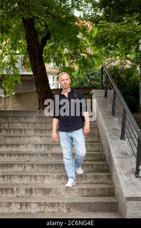 Grauhaariger junger Mann mit Rucksack geht die Treppe im Park hinunter. Stockfoto