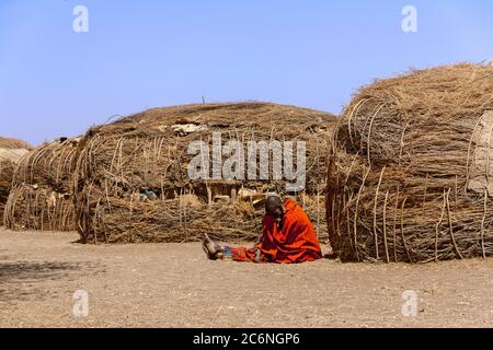 Serengeti, Tansania - September 21. 2012: Eine Massai Frau in rot vor den traditionellen Hütten in einem Massai Dorf im Serengeti National Pa Stockfoto