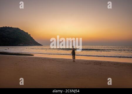 Junge Frau macht Übungen mit einem Holzstock am Strand in Südindien. Orange Sonnenuntergang ar Indischer Ozean . unkenntlich Person Stockfoto