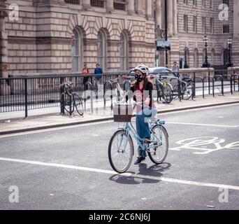 Frau mit Gesichtsbedeckung auf einem Fahrrad an der Ampel in London während der covid-19 Pandemie. Stockfoto