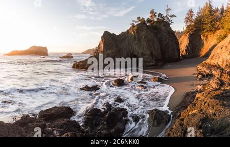 Wunderschöner Sonnenuntergang in Secret Beach Oregon mit einem sanften warmen Glanz auf den Felsen und immergrünen Bäumen auf den Inseln, die diesen Strand so kennungswert machen Stockfoto