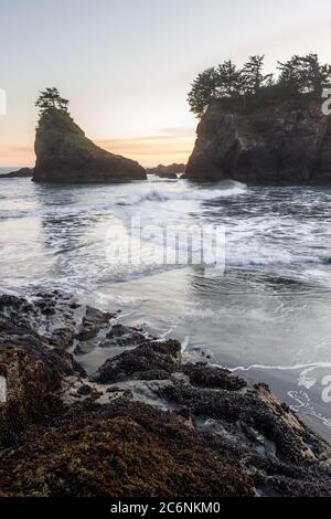 Die Sonne geht am Secret Beach an der südlichen Küste von Oregon bei Sonnenuntergang unter, mit seinen vielen Inselchen, die mit immergrünen Bäumen und verschwommenen Wellen übersät sind Stockfoto
