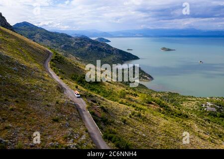 Auto mit zwei Kajkas Fahren auf einer schmalen Bergstraße am Rande einer Klippe am Südufer des Skadar-Sees, Montenegro Stockfoto