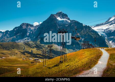 Seilbahn von Grindelwald nach First in der Nähe der Bergstation im Sommer und Panoramablick auf schneebedeckte Berge und Gletscher im Hintergrund. Jungfra Stockfoto