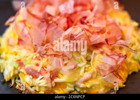 Nahaufnahme eines Omelettes aus Okonomiyaki, das nach Ihren Wünschen zubereitet wird, mit zerkleinerten Kohl zubereitet und mit getrockneten Bonit-Spänen bedeckt ist Stockfoto