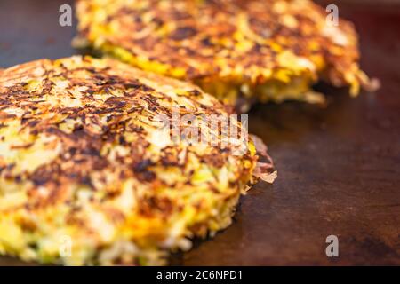 Nahaufnahme eines Omelettes aus Okonomiyaki, das nach Ihren Wünschen zubereitet wird, mit zerkleinerten Kohl zubereitet und beidseitig auf einer heißen Platte gekocht wird. Stockfoto