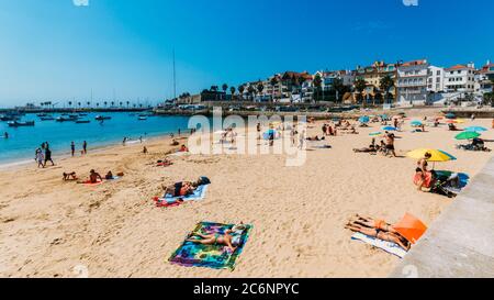 Praia da Ribeira Strand in Cascais, Portugal mit historischen und kommerziellen Gebäuden in der Ferne und Menschen Stockfoto