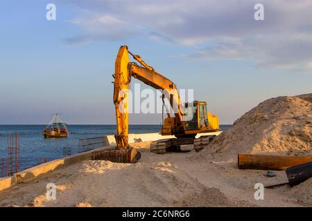 Ein Bagger in der Nähe des Meeres gräbt Sand, um einen Strand an der Küste zu bauen. Stockfoto