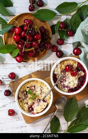 Hausgemachtes Sommerdessert. Kirschbröseln in Backform auf einer Holzplatte. Draufsicht flach lagen Hintergrund. Stockfoto