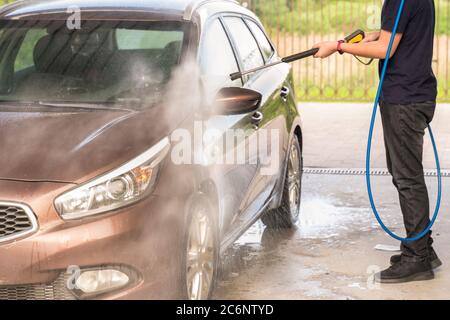 Ein Mann wäscht ein braunes Auto mit einer Pistole zum Waschen von Hochdruckautos Stockfoto