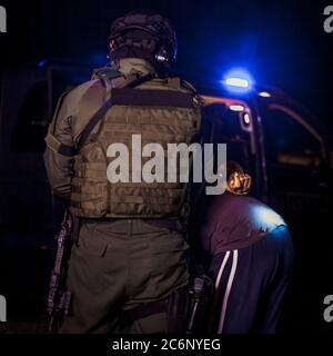 Ein Polizeibeamter legt einem Verbrecher während einer Festnahme Handschellen an die Hände. Polizeiauto mit blinkenden Leuchttürmen Stockfoto