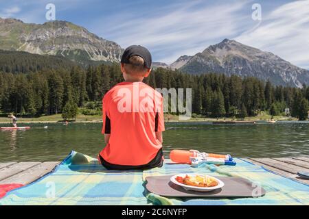 Junge sitzt auf einer Holzpromenade und schaut auf einen See Stockfoto
