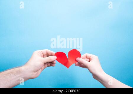 Weibliche und männliche Hand brechen ein Papier roten Herz auf einem blauen Hintergrund mit Platz für Text. Beziehungsprobleme Stockfoto