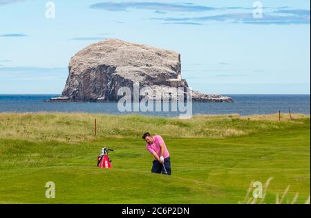 North Berwick, East Lothian, Schottland, Großbritannien, 11. Juli 2020. UK Wetter: Ein sehr luftiger sonniger Tag in der Küstenstadt am Ufer des Firth of Forth. Die Bass Rock Gannet Kolonie ist in der Sonne beleuchtet mit Blick über den Glen Golfplatz, während ein männlicher Golfer eine Schaukel nimmt Stockfoto