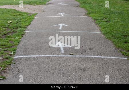 Soziale Distanzierungspfeile bei Coronavirus-Pandemie auf dem Weg mit Gras Stockfoto