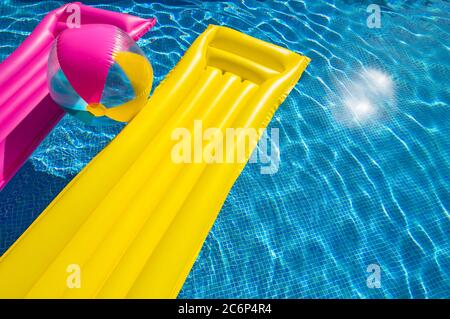Gelb und rosa aufblasbare Luftmatratze mit bunten Strandball schwimmend am Pool Wasser Stockfoto