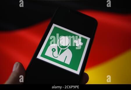 Viersen, Deutschland - 9. Juli. 2020: Blick auf isolierte Handy-Bildschirm mit internationalen Gesundheits-und Arzt Symbol. Verschwommene, winkende deutsche Flagge Stockfoto