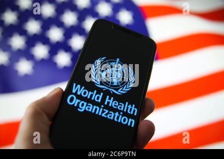 Viersen, Deutschland - 9. Juli. 2020: Logo der Weltgesundheitsorganisation (WHO) auf dem Handy-Bildschirm mit menschlicher Hand. Verschwommene winkende Flagge der USA-Backgro Stockfoto