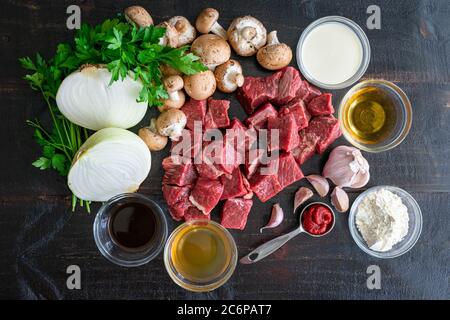 Steak Diane Auflauf Zutaten: Rohes Rindfleisch, Gemüse und Gewürze auf dunklem Holz Hintergrund Stockfoto