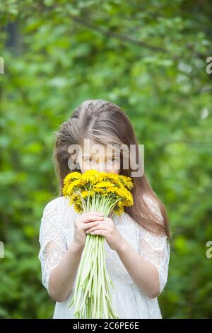 Modische Mädchen in einem hellen Kleid Posen und hält einen großen Strauß von gelben Löwenzahn Stockfoto