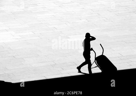 Silhouette eines Mannes, der eine Schubkarre auf dem Bürgersteig leert, in kontrastreicher Schwarz-Weiß-Ansicht mit hohem Winkel Stockfoto