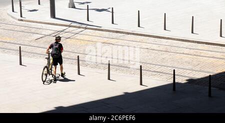 Belgrad, Serbien - 9. Juli 2020: Ein junger Mann, der an einem heißen Sommertag neben seinem Fahrrad unterwegs ist, während er mit der Straßenbahn die Straße überquert, hinten hochgeneigt Stockfoto