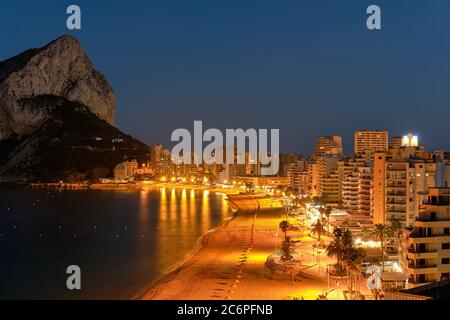 Stadtbild-Panorama von oben auf Calpe. Nachtansicht Straßenlaternen Beleuchtung Strandpromenade. Sandiger leerer Strand Penon de Ifach Felsen. Calpe Stockfoto