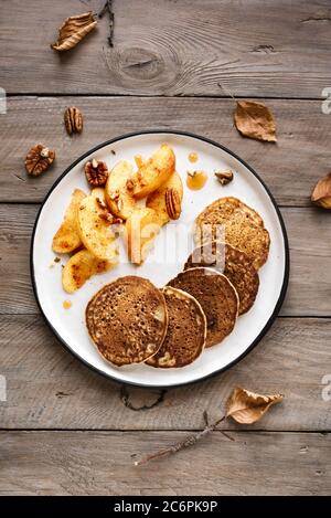 Herbstfrühstück - Pfannkuchen mit karamellisierten Äpfeln, Pekannüssen und Honig auf Holztisch, Draufsicht. Gesunde vegetarische Mahlzeit der Saison. Stockfoto
